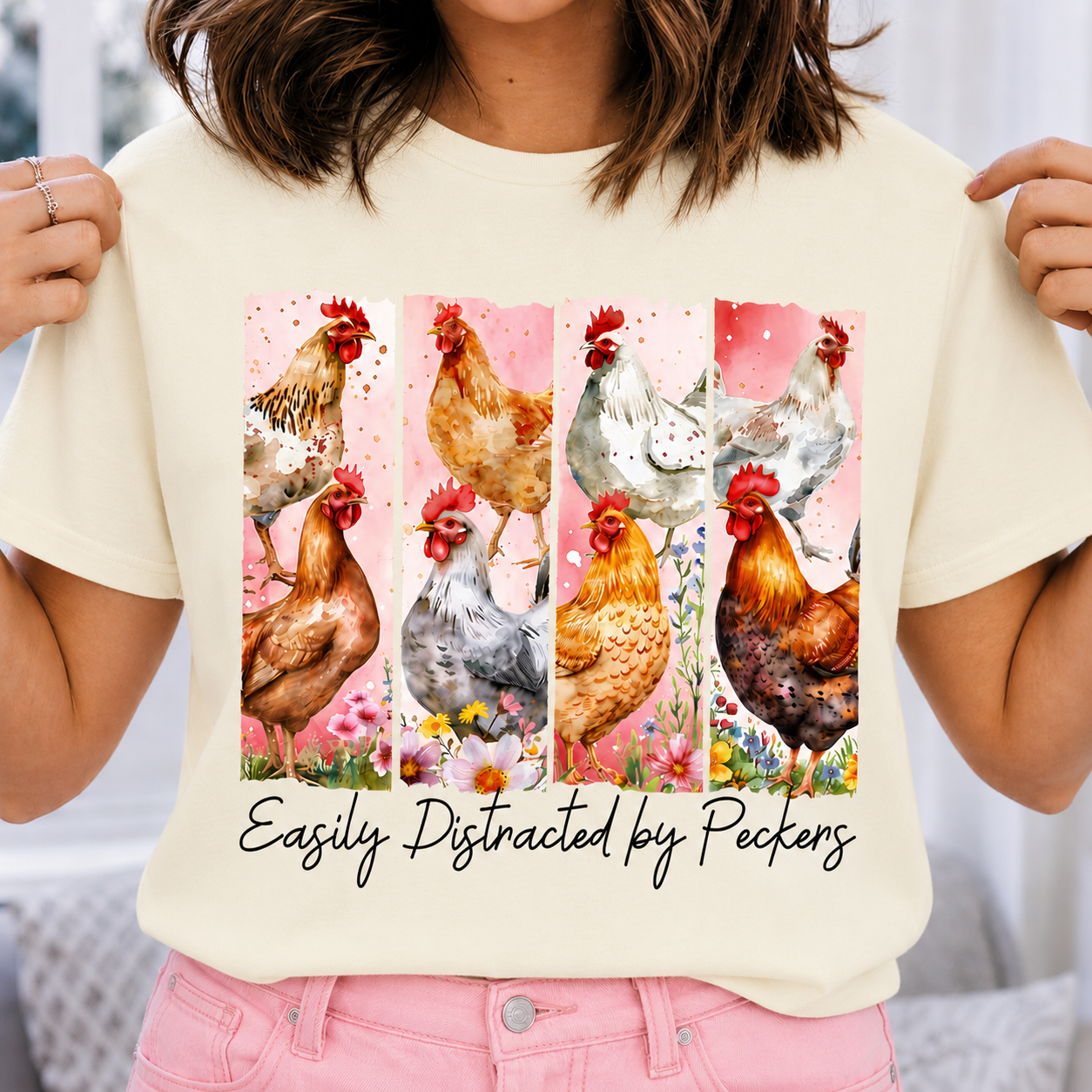 Ivory colored t-shirt with chicken design and text 'Easily Distracted by Peckers' held by a person.