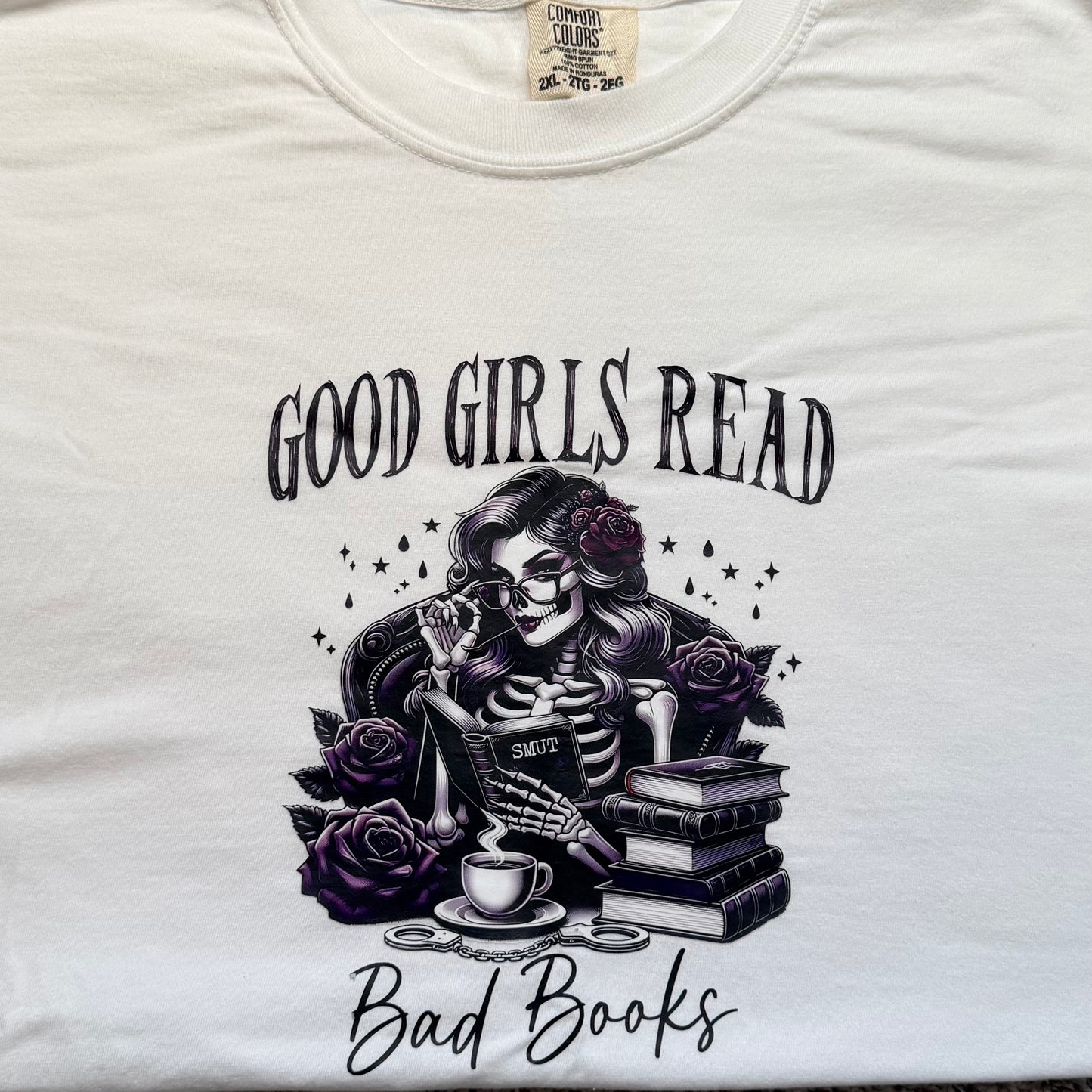 White t-shirt with skeleton design and text 'Good Girls Read Bad Books' on a white background