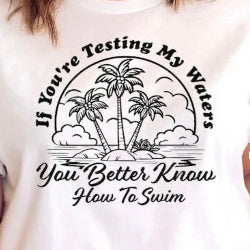 White t-shirt with black graphic and text 'If You're Testing My Waters, You Better Know How To Swim' on a white background.