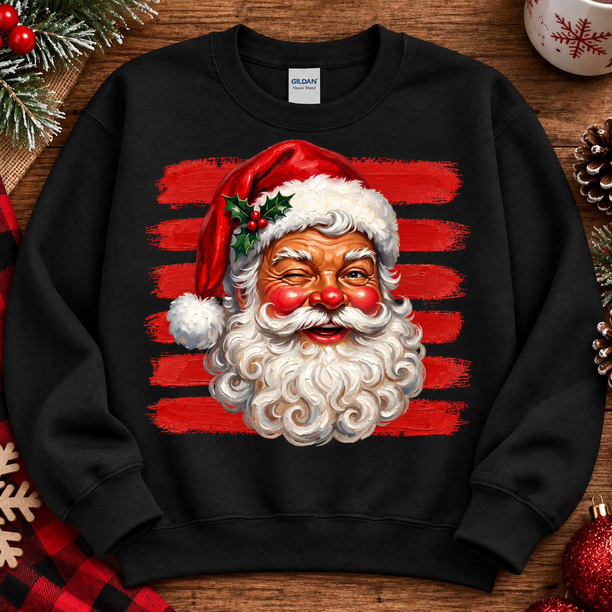 A black crewneck sweatshirt featuring a graphic print of a smiling Santa Claus with a white beard, red nose, and red striped background, styled on a wooden surface with Christmas decorations.