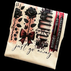 A shirt with a design featuring black roses, a maroon bow, stacked books, and a flickering candle with the text 'just go away' written on it.