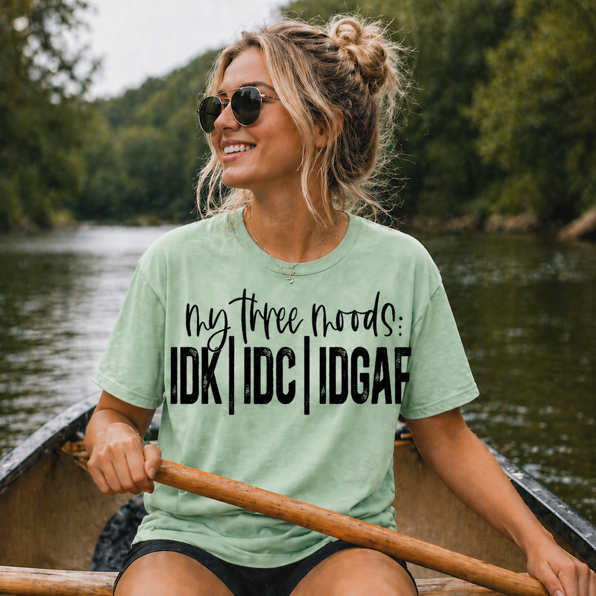 Woman in a canoe wearing a mint green t-shirt with humorous text, surrounded by nature.