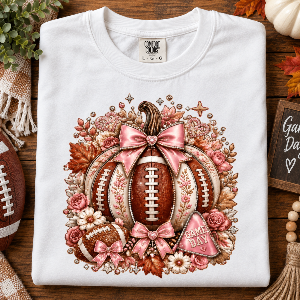 A folded white Comfort Colors t-shirt with a detailed autumn football graphic, displayed on a rustic wooden surface with seasonal props.