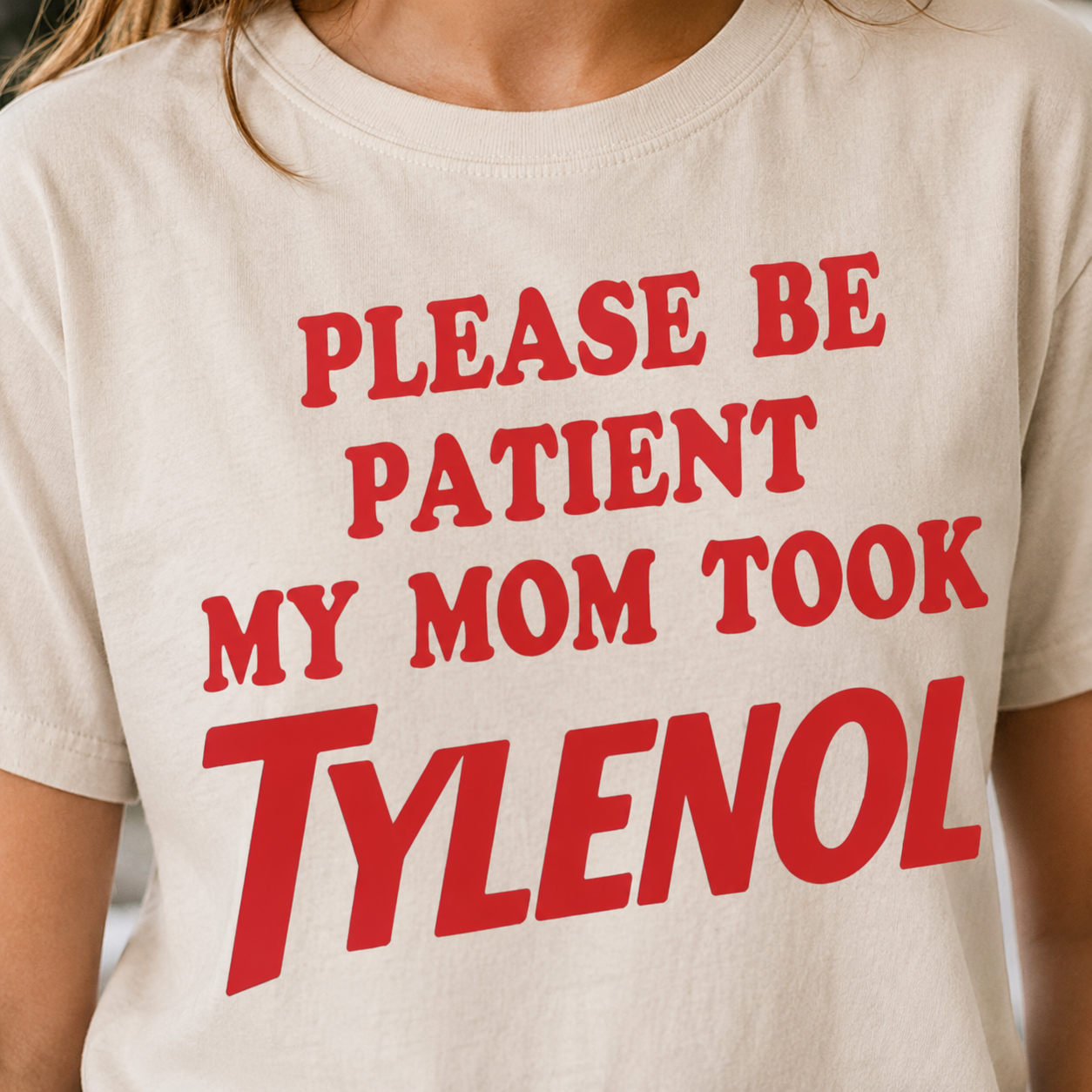 White t-shirt with red text 'PLEASE BE PATIENT MY MOM TOOK TYLENOL' worn by a person.