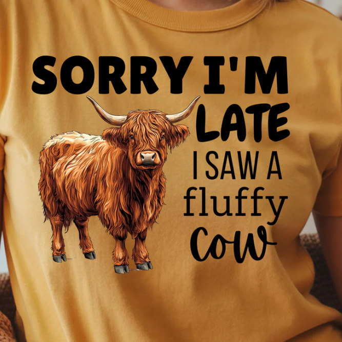 Design closeup of a yellow t-shirt with a fluffy cow graphic and text on a plain background