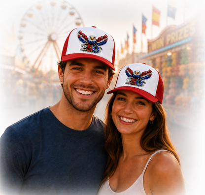 Two people wearing matching red, white, and blue baseball caps with an eagle design, standing in front of a Ferris wheel.