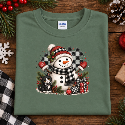 A folded military green Gildan Youth t-shirt with a festive Christmas snowman graphic, displayed on a rustic wooden background with holiday decorations.