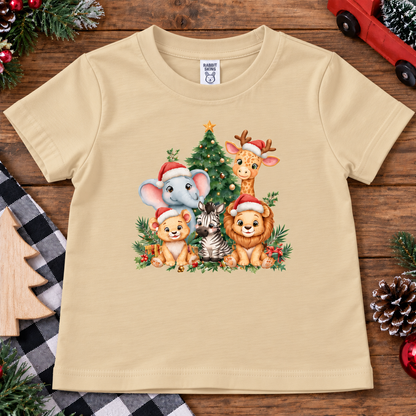 A latte colored short-sleeve kids' t-shirt with a colorful Christmas animal graphic, laid flat on a rustic wooden background with holiday decorations.