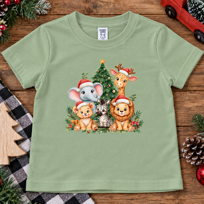 A sage green short-sleeve t-shirt with a colorful Christmas animal graphic, laid flat on a rustic wooden surface surrounded by holiday decorations.