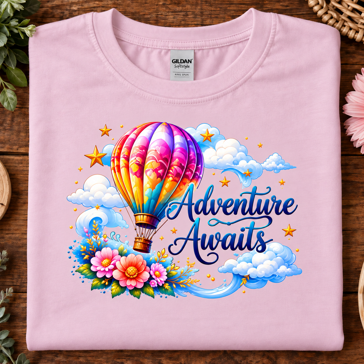 Light pink colored t-shirt with a hot air balloon flying in the clouds with the text Adventure Awaits