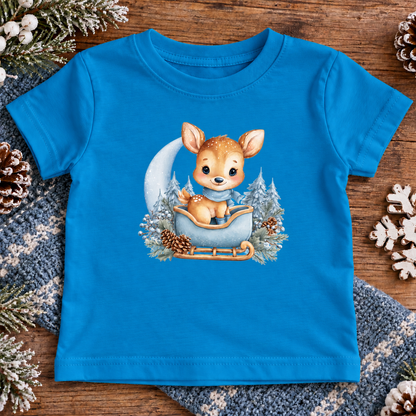 A cobalt colored toddler t-shirt with a baby deer sitting in a sleigh surrounded with trees and pinecones