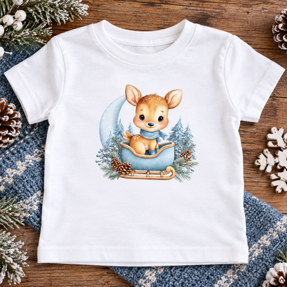 A white short-sleeve baby t-shirt decorated with a winter-themed graphic of a cute deer in a blue sleigh surrounded by pine trees and pinecones. 
