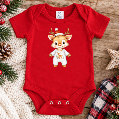 A red short-sleeve baby bodysuit laid flat on a rustic wood surface, decorated with holiday props including pine branches, a star, a plaid cloth, and red berries. The bodysuit has a cartoon reindeer graphic on the chest wearing a Santa hat and white outfit.