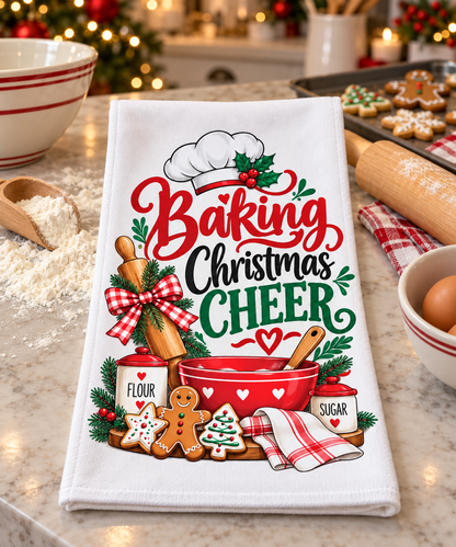 A white kitchen towel with a festive Christmas baking design, featuring the text 'Baking Christmas CHEER' in red and green lettering with illustrations of a chef's hat, rolling pin, red mixing bowl, gingerbread cookies, and flour and sugar containers, displayed on a kitchen counter.