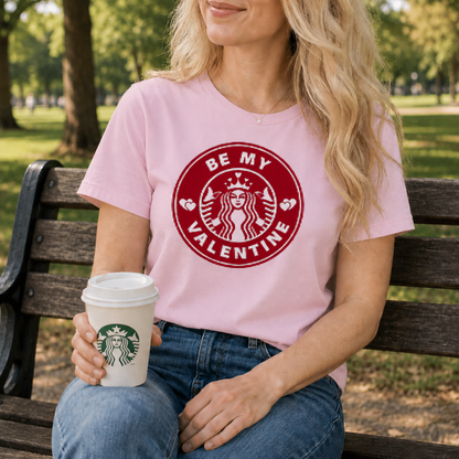 Person wearing a pink t-shirt with a Valentine's Day design, sitting on a bench outdoors.
