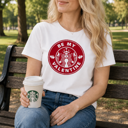 Person wearing a white t-shirt with a red Starbucks logo and holding a coffee cup on a park bench.