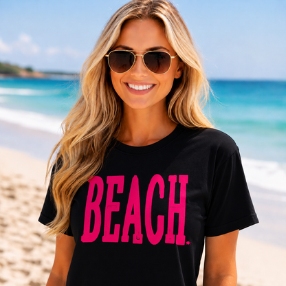 Woman wearing a black colored t-shirt with 'BEACH' in pink on a beach.