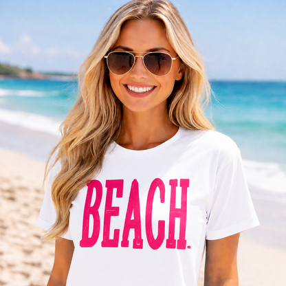 Woman wearing a white colored t-shirt with 'BEACH' in pink on a beach.