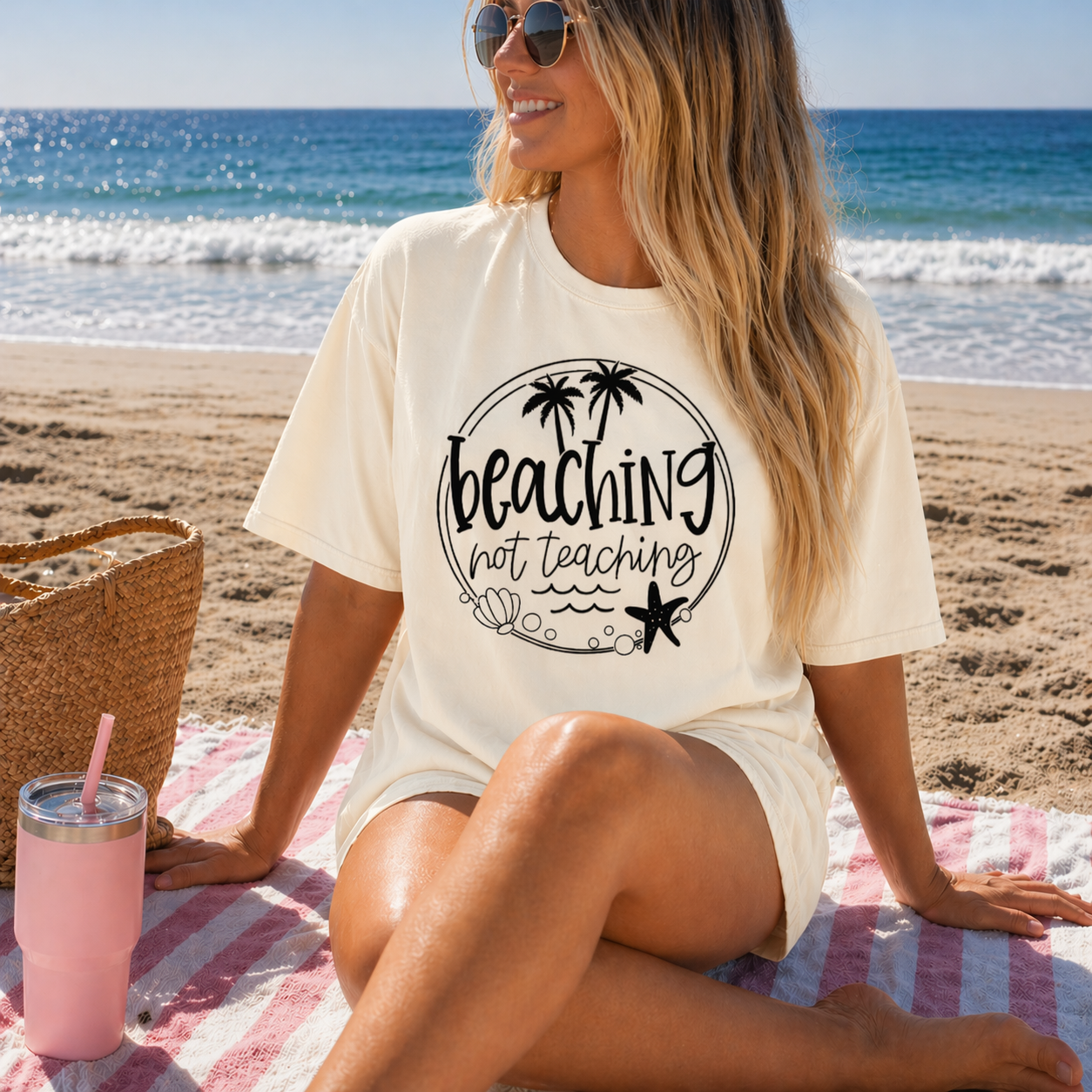 Woman sitting on a beach with a ivory shirt that says 'Beaching not teaching'.