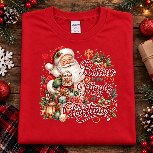 A red t-shirt with a Santa with hot cocoa and presents with text Believe in the Magic of Christmas