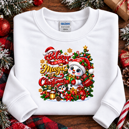 A folded white Gildan sweatshirt with a colorful Christmas graphic print featuring pandas, a Santa hat, ornaments, and the text 'Believe in the Magic of Christmas,' styled on a rustic wooden surface with holiday decorations.