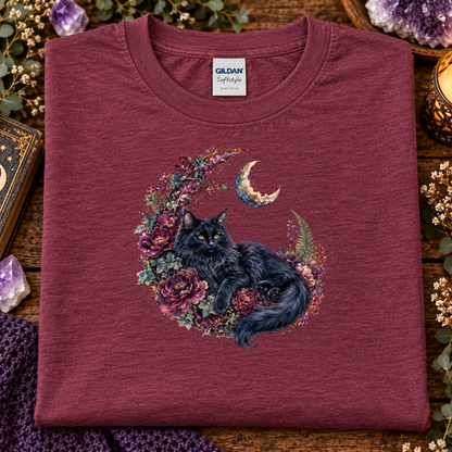 A folded heathermaroon Gildan Softstyle t-shirt features a graphic of a fluffy black cat curled up inside a crescent moon wreath decorated with purple and pink flowers.