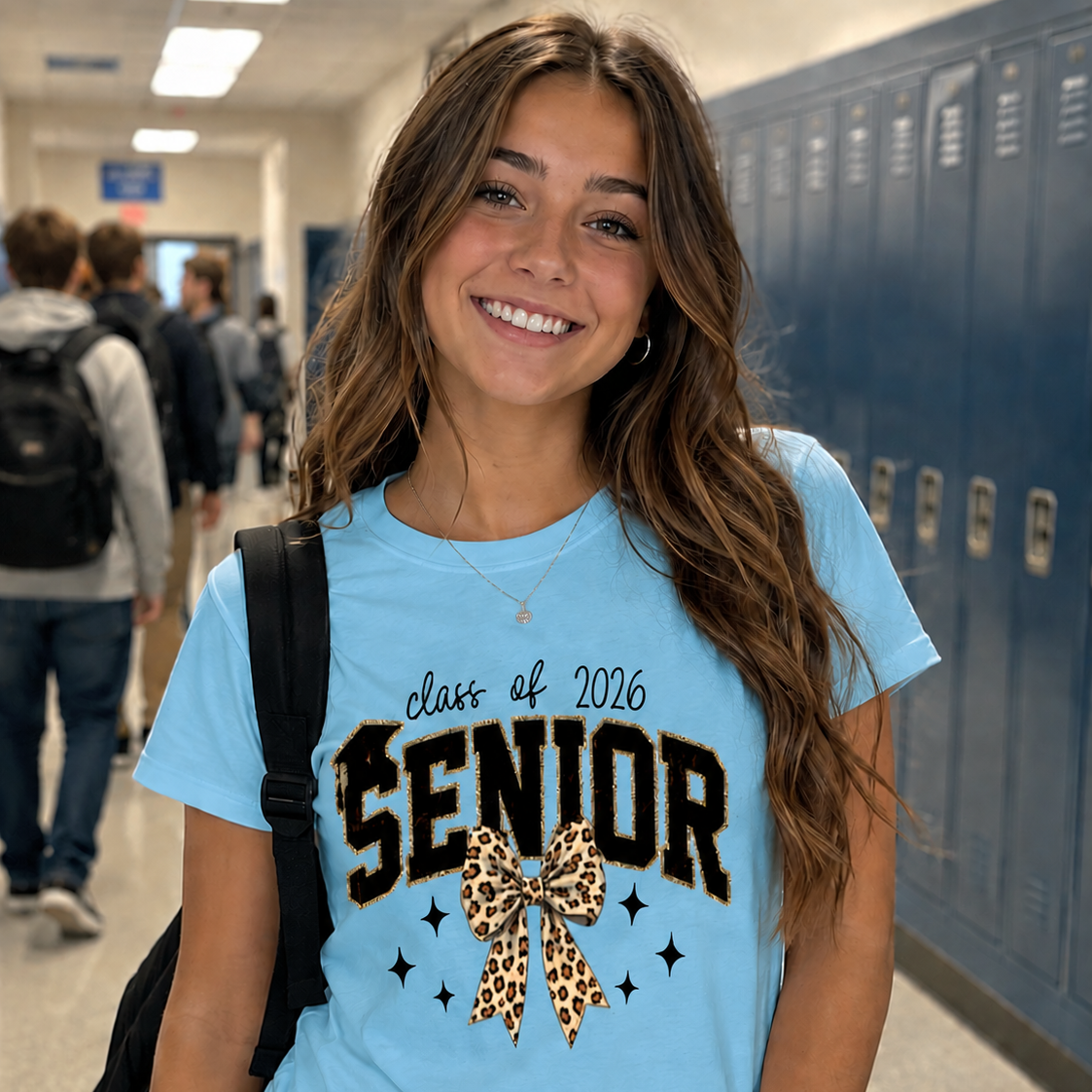 Young woman wearing a 'class of 2026 Senior' sky blue t-shirt in a school hallway.
