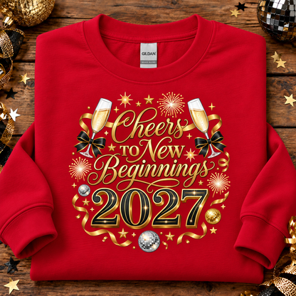 A red Gildan crewneck sweatshirt laid flat on a rustic wooden surface, decorated with a festive gold and black graphic that reads 'Cheers to New Beginnings 2027' with champagne glasses, ribbons, stars, and disco balls.