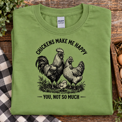 A folded kiwi green t-shirt with a black graphic of a rooster, hen, and chick, accompanied by the text 'CHICKENS MAKE ME HAPPY YOU, NOT SO MUCH'. The shirt is displayed on a rustic wooden background with a plaid cloth and greenery.