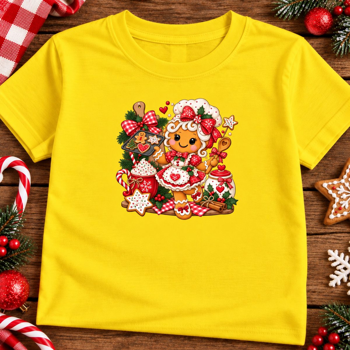 A daisy yellow short-sleeve t-shirt with a colorful Christmas gingerbread-themed graphic print, laid flat on a rustic wooden background surrounded by holiday decorations like candy canes, pine branches, and red ornaments.