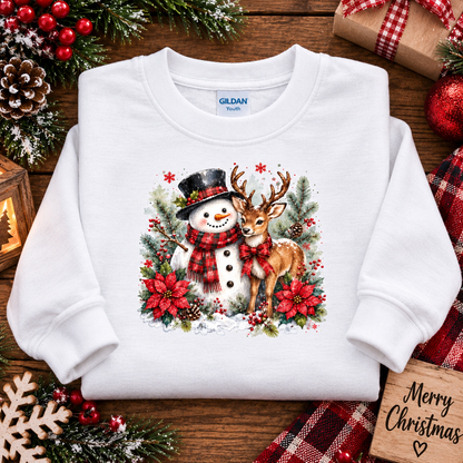 A white Gildan Youth crewneck sweatshirt featuring a festive Christmas graphic of a snowman and a deer, styled in a flat-lay on a wooden surface with holiday decorations.