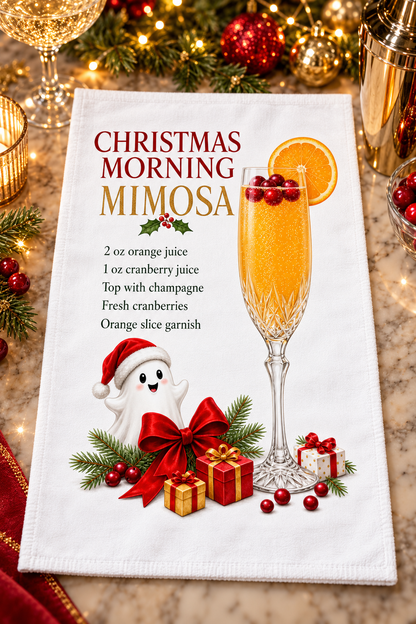 A white kitchen towel with a festive Christmas morning mimosa recipe and graphic design displayed on a marble countertop with holiday decorations in the background.