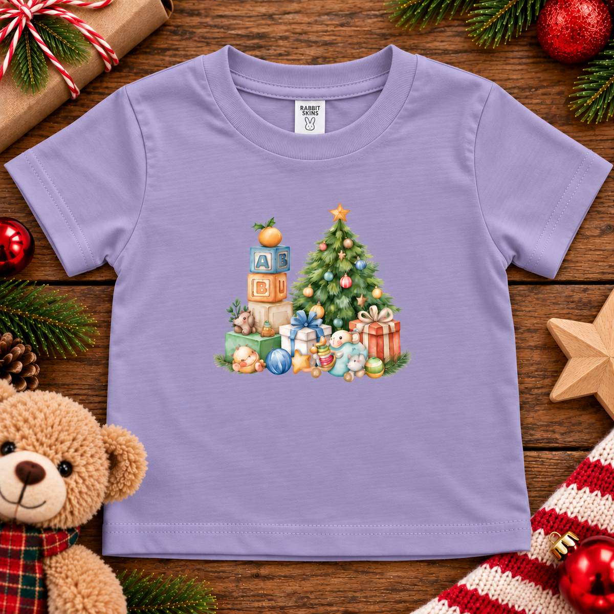A lavender colored toddler t-shirt with a Christmas graphic with a tree, blocks and presents