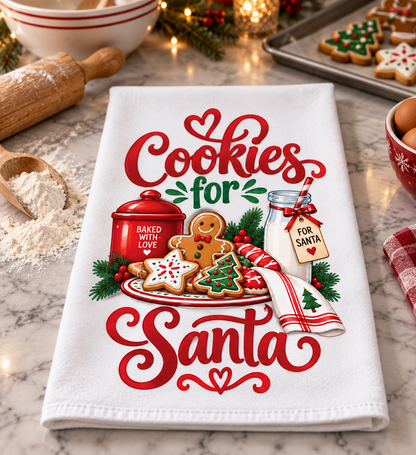 A white kitchen tea towel laid on a marble countertop, printed with the phrase 'Cookies for Santa' in red script and surrounded by holiday cookie and gingerbread illustrations. The scene includes baking props like a rolling pin, flour, a mug, and cookies in a warm, styled kitchen setting.