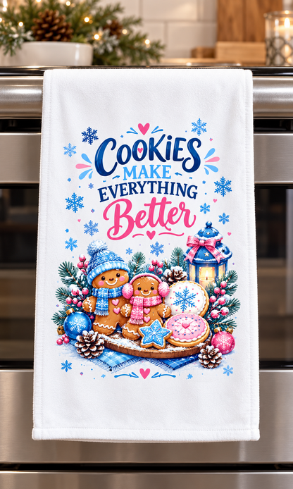 A white kitchen towel hanging on a stainless steel oven handle, featuring a festive Christmas cookie illustration with gingerbread men, snowflakes, pinecones, and the text 'Cookies Make Everything Better'.