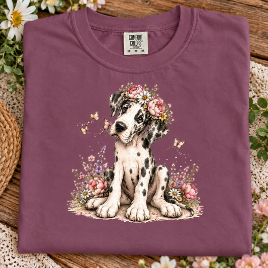 A folded berry purple Comfort Colors t-shirt featuring a watercolor-style graphic of a Dalmatian puppy wearing a pink flower crown, displayed on a rustic wooden surface with decorative flowers and lace.