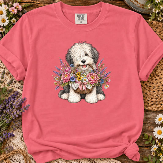 A watermelon colored t-shirt with an old english sheepdog sitting and holding a wicker basket overflowing with pink peonies, blue flowers, yellow daisies, and a pink bow graphic design.