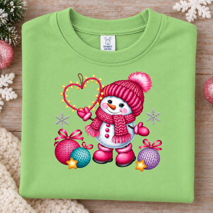 A folded keylime green crewneck sweatshirt with a colorful Christmas snowman graphic, displayed on a wooden surface with festive decorations.