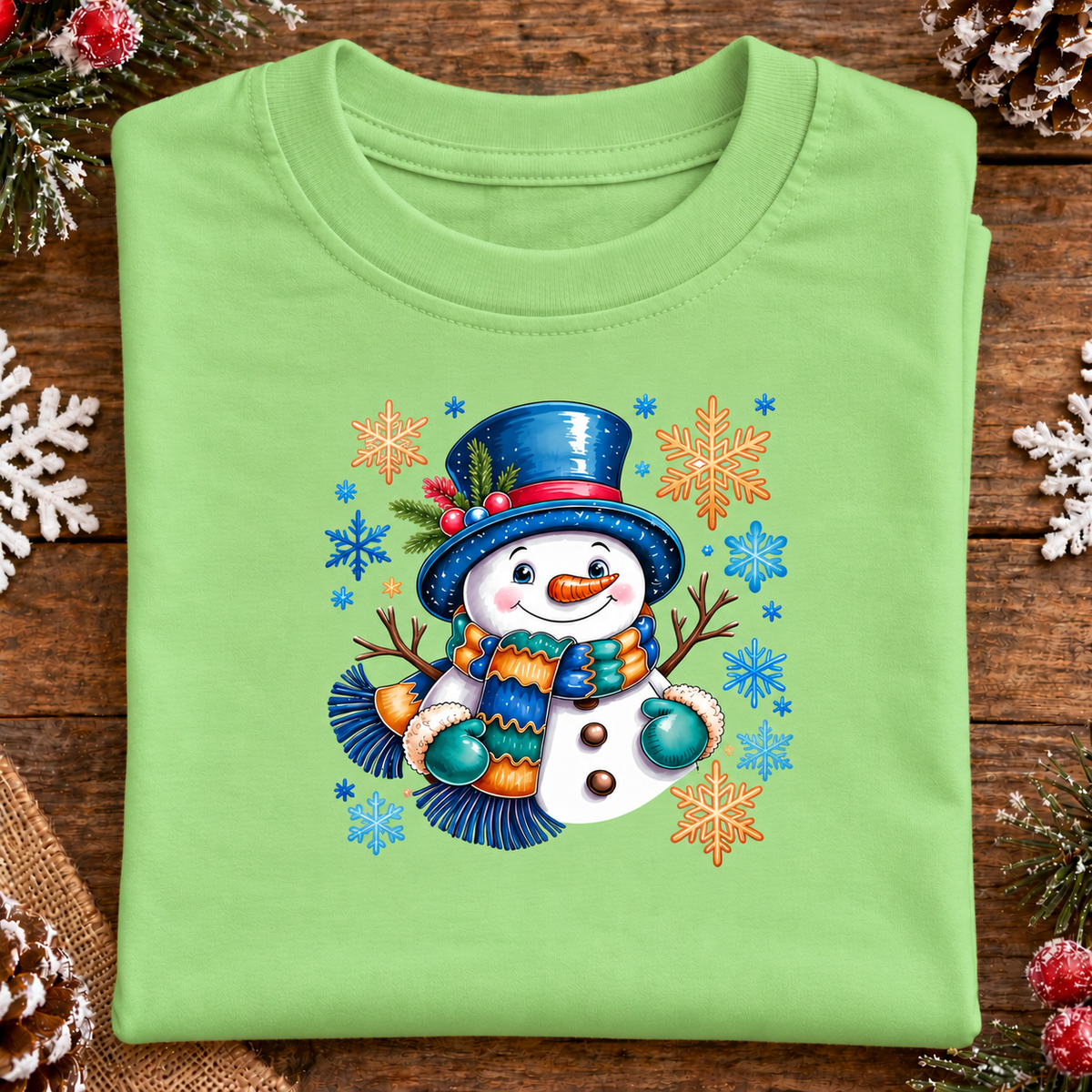 A folded keylime green crewneck t-shirt with a colorful Christmas snowman graphic, displayed on a rustic wooden surface decorated with white snowflakes and pinecones.