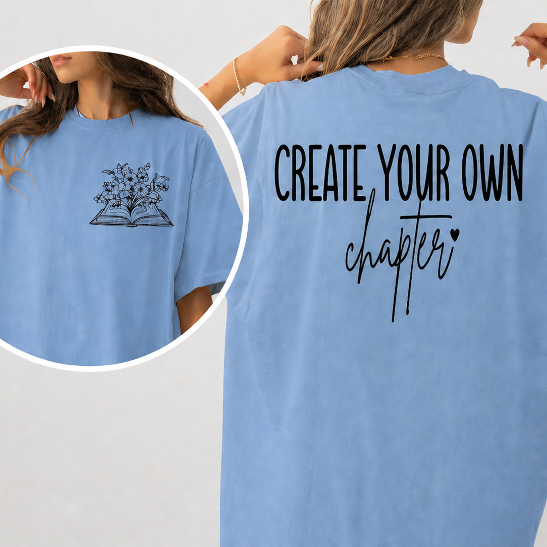Light blue t-shirt with 'Create Your Own Chapter' text on the back, worn by a person.