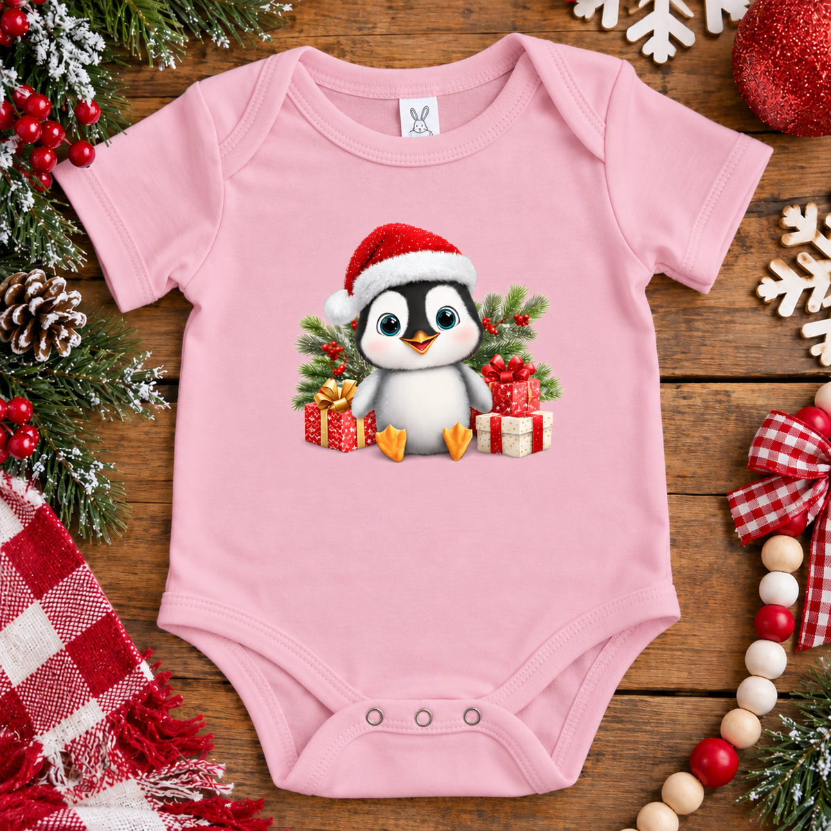 A pink onesie with a penquin with a santa hat on and surrounded by presents
