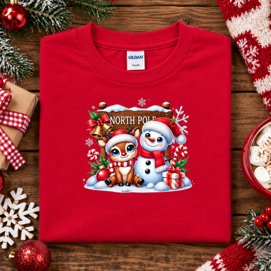 A red t-shirt with a christmas graphic design of a North Pole sign with a reindeer and snowman in festive scene
