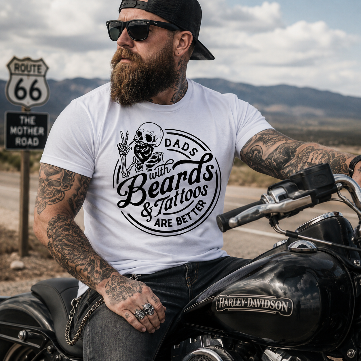 Man with tattoos and a beard sitting on a motorcycle wearing a t-shirt with a graphic design.