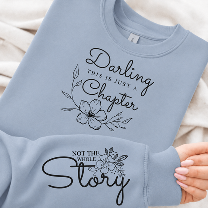 Light blue sweatshirt with floral text design held by a hand.