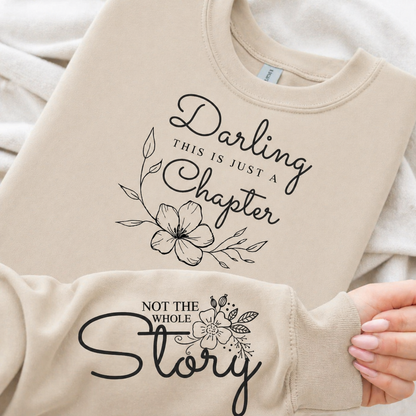 Sand colored sweatshirt with black floral text design held by a hand.