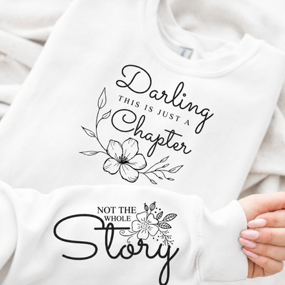 White sweatshirt with black text and floral designs, held by a person.