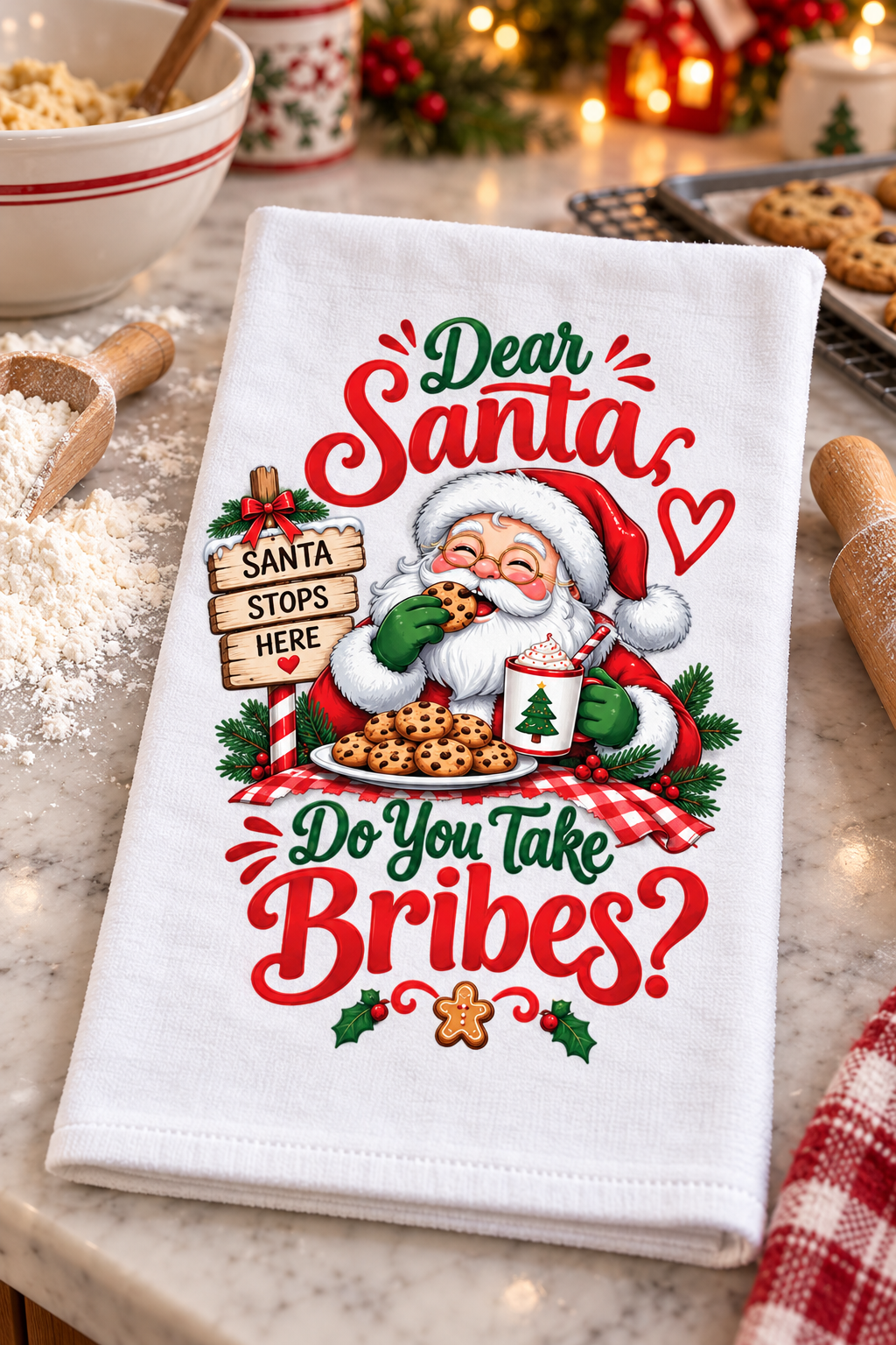 A white kitchen tea towel with a festive Christmas design featuring Santa Claus, cookies, holly, and the text 'Dear Santa Do You Take Bribes?' laid on a marble countertop with baking props in the background.
