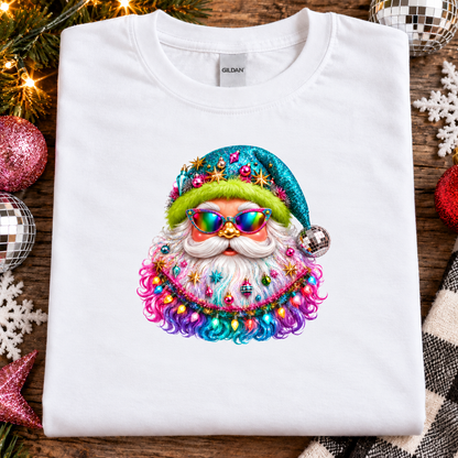 A folded white Gildan t-shirt with a colorful, glittery Santa Claus graphic on the front, styled on a rustic wooden background with Christmas ornaments and lights.
