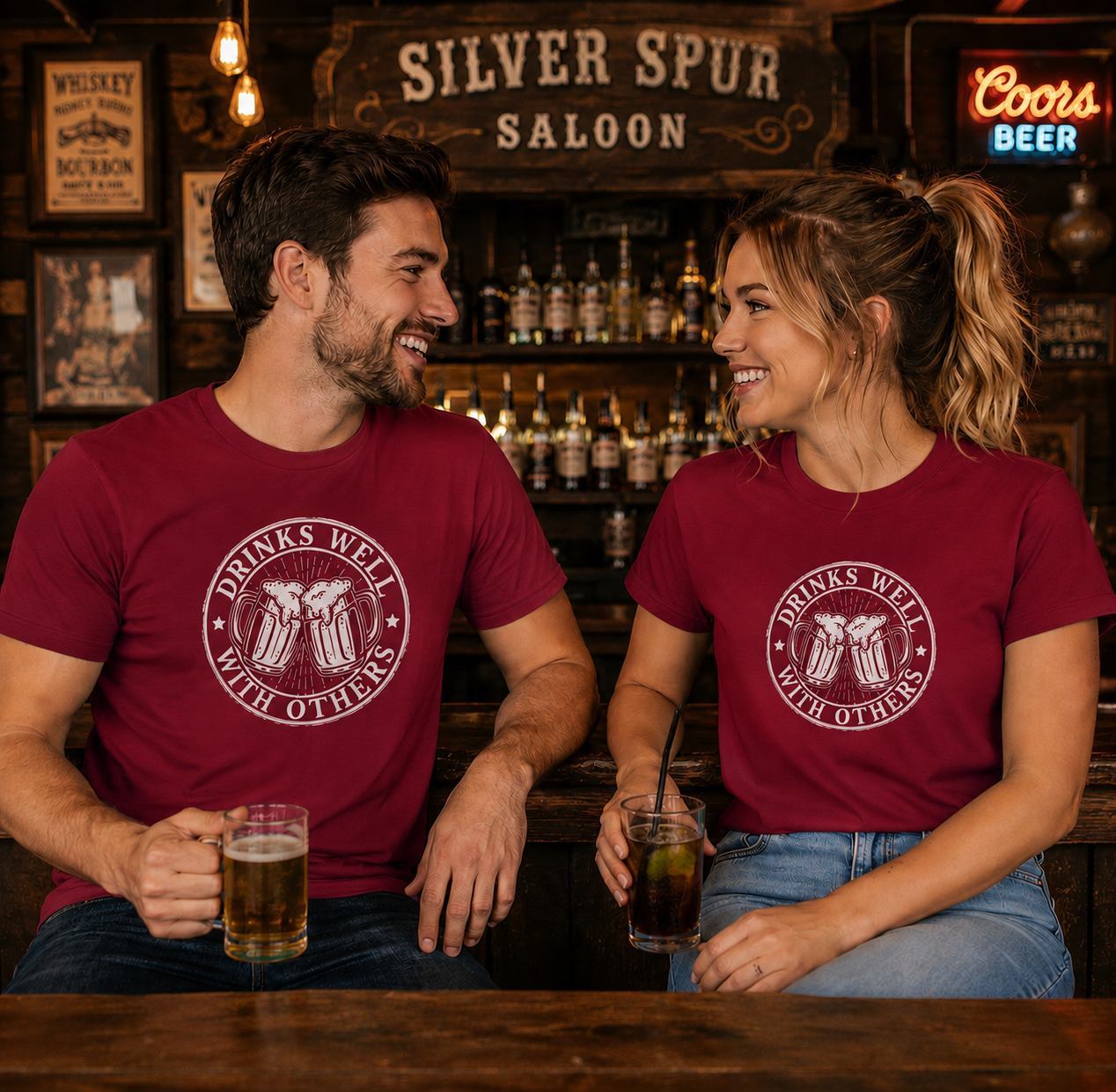 Two people sitting at a bar wearing matching red t-shirts with a logo and text, enjoying drinks.