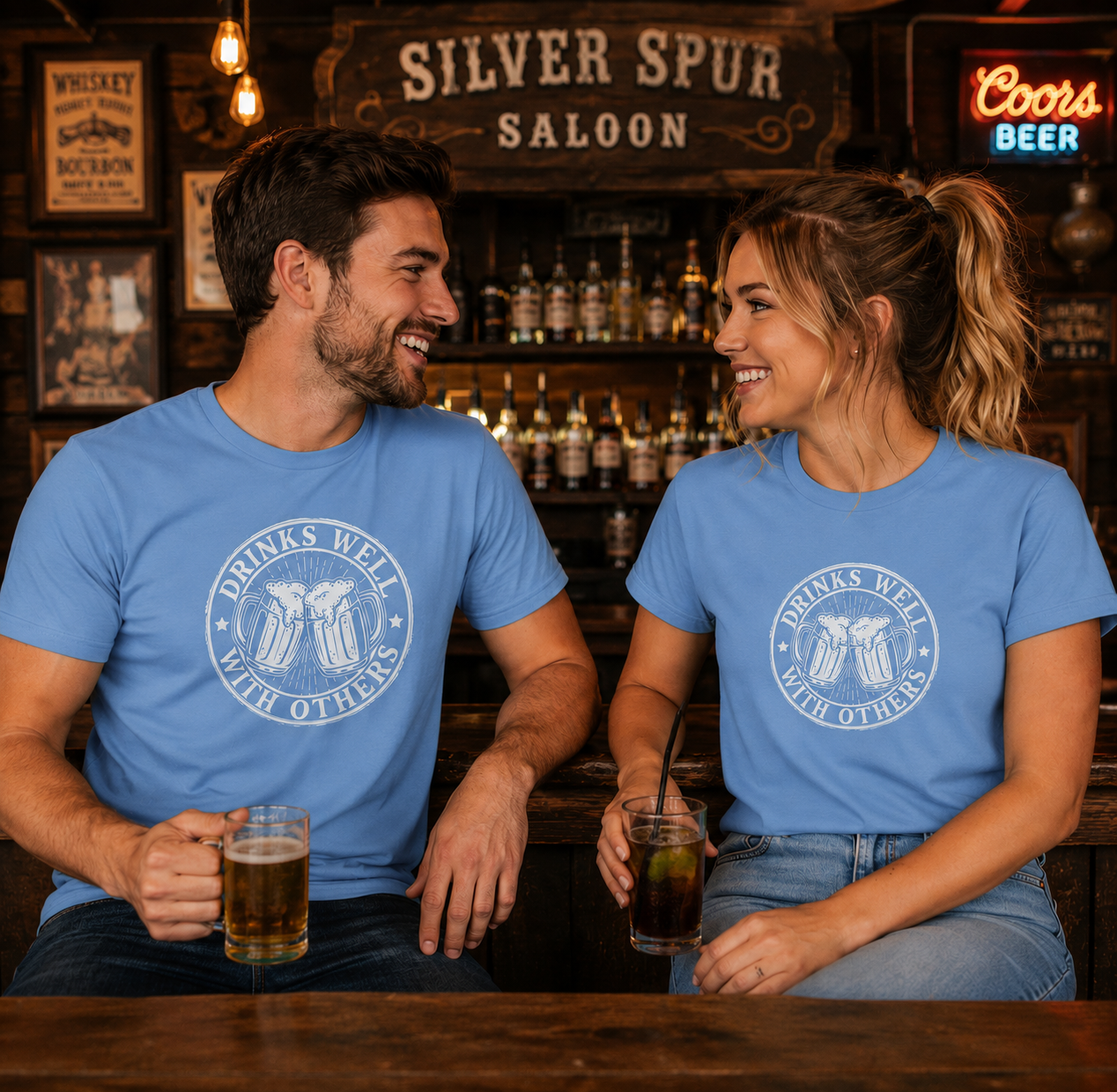 Two people sitting at a bar wearing matching blue t-shirts with a logo and text, enjoying drinks.